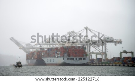 OAKLAND, CA - OCTOBER 20, 2014: Port of Oakland, shipping containers being loaded on Cosco Phillipines ship in the fog and rain. Cosco Container lines provides world wide shipping services year round.