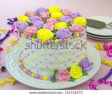Pastel Rainbow Yellow, Pink, Purple butter cream frosting handmade roses on a round cake frosted with white icing and embellished with yellow, pink and purple dots of buttercream frosting.