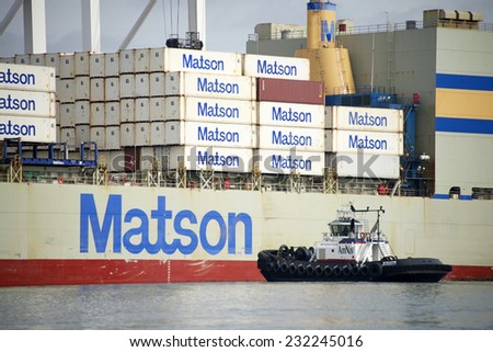 OAKLAND, CA - NOVEMBER 21, 2014: American Navigation (AmNav) Tugboat Revolution, a Dolphin class tractor tug, approaches Matson Cargo Ship Mokihana prior to assisting to maneuver the ship out of port.