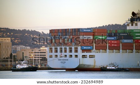 OAKLAND, CA - NOVEMBER 23, 2014: Tug Boat AMERICA pulling from the stern while Tug Boat ASTORIA pushes the Starboard quarter to turn COSCO KAOHSIUNG Cargo Ship 180 degrees to exit the Port of Oakland.