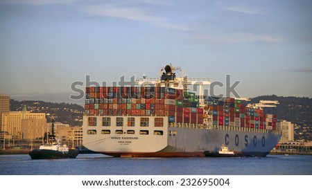 OAKLAND, CA - NOVEMBER 23, 2014: Tug Boat AMERICA pulling from the stern while Tug Boat ASTORIA pushes the Starboard quarter to turn COSCO KAOHSIUNG Cargo Ship 180 degrees to exit the Port of Oakland.