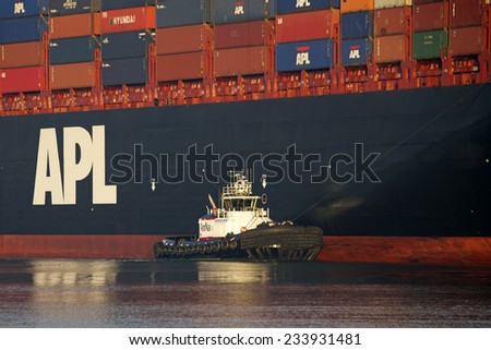 OAKLAND, CA - NOVEMBER 27, 2014:  American Navigation (AmNav) Tugboat REVOLUTION off the Starboard side of  American President Lines (APL) Cargo ship PARIS assisting it out of the Port of Oakland.