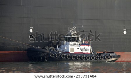 OAKLAND, CA - NOVEMBER 27, 2014: American Navigation (AmNav) Tugboat REVOLUTION escorting a Cargo Ship. Tugs move vessels that should not move themselves, such as large ships in a crowded harbor.