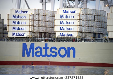 OAKLAND, CA - DECEMBER 12, 2014: A lone paddle boarder passes the Matson Cargo Ship MAHIMAHI loading at the Port of Oakland. Many people use the inner harbor for recreational water activities.
