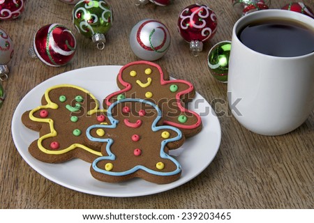 Gingerbread cookie men on a plate with a cup of coffee and Christmas Ornaments in the background on a wood table