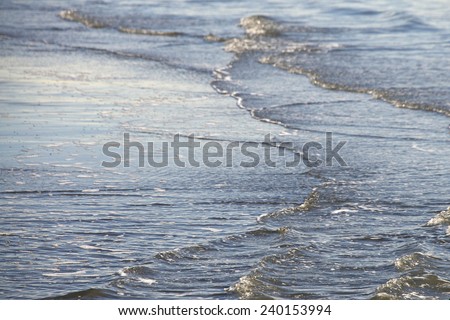 Gentle waves rolling in from several directions on a small secluded sandy beach during low tide. Relaxing background image.