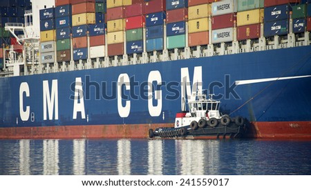 OAKLAND, CA - JANUARY 04, 2014: Tugboat VETERAN off the Starboard side of CMA CGM Cargo Ship CENTAURUS, working with multiple tugboats to guid the ship away from the Port of Oakland.