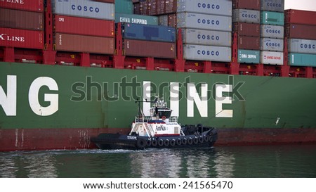 OAKLAND, CA - JANUARY 04, 2014: AmNav Tugboat Revolution assisting China Shipping Line Ship XIN YA ZHOU out of the Port of Oakland. A tugboat maneuvers vessels by pushing or towing them.