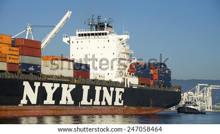 OAKLAND, CA - JANUARY 25, 2015: Tractor Tugboat ABRA FRANCO, at the stern of NYK Cargo Ship NEBULA guiding the ship out of the Port of Oakland. A tugboat maneuvers vessels by pushing or towing them.