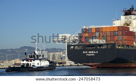 OAKLAND, CA - JANUARY 25, 2015: Tractor Tugboat AHBRA FRANCO, at the stern of NYK Cargo Ship NEBULA guiding the ship out of the Port of Oakland. A tugboat maneuvers vessels by pushing or towing them.