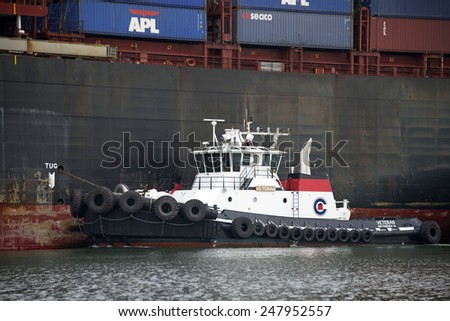 OAKLAND, CA - JANUARY 27, 2015: Tugboat VETERAN off the Port side of APL THAILAND as the Ship enters the Port of Oakland. Tugboats are vital for safe, efficient entry and exit for the large ships.