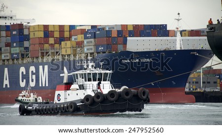 OAKLAND, CA - JANUARY 27, 2015: A tugboat maneuvers vessels by pushing or towing them. Tugboat VETERAN at the Stern of a Cargo Ship as it enters the Port of Oakland.