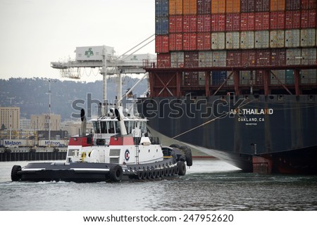 OAKLAND, CA - JANUARY 27, 2015: Tugboat DELTA CATHYRN guiding from the Stern of APL THAILAND as it enters the Port of Oakland. Tugboats are vital for safe, efficient entry and exit for the large ships