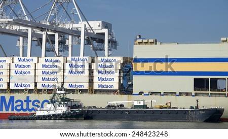 OAKLAND, CA - JANUARY 28, 2015: Tugboat POINT FERMIN pushing a Barge Ship next to Matson Cargo Ship MOKIHANA. Crews will utilize the barge to provide maritime services to the vessel.