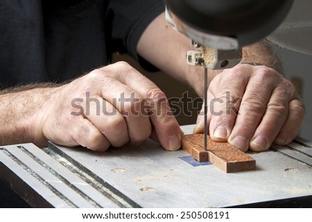 Male hands holding a small piece of wood precision cutting on a table top jig saw. Saw dust everywhere.