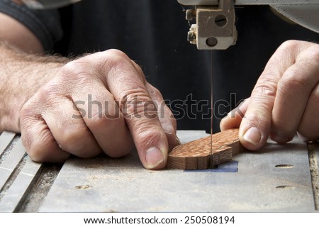 Male hands holding a small piece of wood precision cutting on a table top jig saw. Saw dust everywhere.
