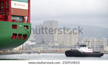 OAKLAND, CA - FEBRUARY 07, 2015: AmNav Tugboat REVOLUTION at the Stern of CSCL Cargo Ship YELLOW SEA assisting the ship enter the Port of Oakland. A tugboat maneuvers vessels by pushing or towing them