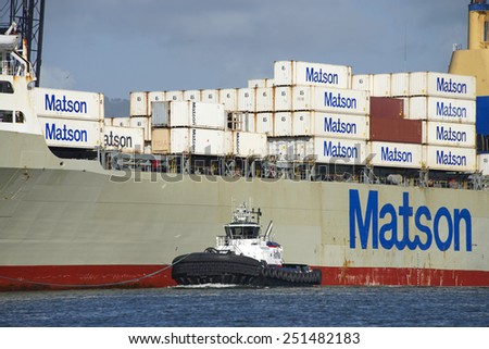 OAKLAND, CA - FEBRUARY 09, 2015: AmNav Tugboat REVOLUTION on the Port side of Matson Cargo Ship MANOA as it enters the Port of Oakland. A tugboat maneuvers vessels by pushing or towing them.