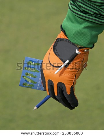 Male hand with golf score card keeping score. Holding the score card off to the side while his buddies golf, ready to keep track