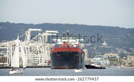 OAKLAND, CA - MARCH 21, 2015: APL Cargo Ship CHINA entering the port of Oakland with Tugboat VETERAN assisting from the Port Bow. Multiple sail boats cross in front of the ship.