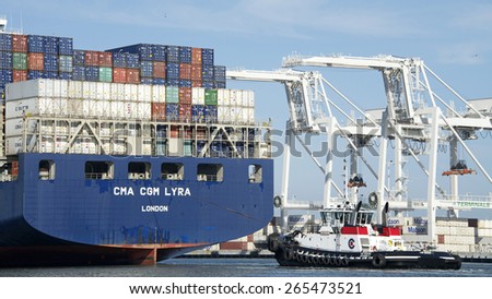 OAKLAND, CA - MARCH 30, 2015: Tugboat VETERAN at the Stern of CMA CGM LYRA assisting the vessel enter the Port of Oakland. Tugboats are vital for safe, efficient entry and exit for the large ships.