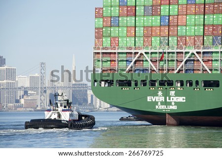 OAKLAND, CA - APRIL 04, 2015: AmNav Tugboat REVOLUTION assisting EVER LOGIC to the Port of Oakland from the stern. Tugs move vessels that should not move themselves, such as ships in a crowded harbor.