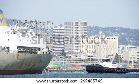 OAKLAND, CA - APRIL 13, 2015: REVOLUTION at the stern of Cargo Ship MAUI, assisting it to maneuver into the Port of Oakland. Tugboats are vital for safe, efficient entry and exit for the large ships.