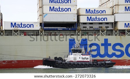 OAKLAND, CA - APRIL 22, 2015: AmNav Tugboat PATRICIA ANN on the port side of Matson Cargo Ship MOKIHANA, assisting it to maneuver into the Port of Oakland.