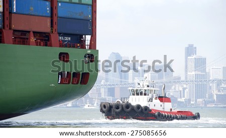 OAKLAND, CA - MAY 03, 2015: Tugboat VALOR off the stern of CSCL SPRING, assisting the vessel to maneuver into the Port of Oakland. San Francisco City in the background.