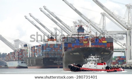 OAKLAND, CA - MAY 14, 2015: Tugboat VALOR maneuvers across the bow to push APL Cargo Ship TURQUOISE away from the docks, assisting with the vessels departure from the Port of Oakland.