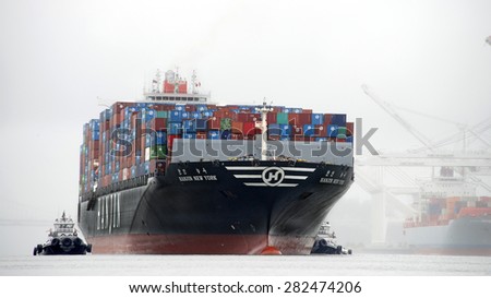 OAKLAND, CA - MAY 26, 2015:  HANJIN NEW YORK entering the Port of Oakland with tugboats assisting the vessel to maneuver through fog and rain. A tugboat maneuvers vessels by pushing or towing them.