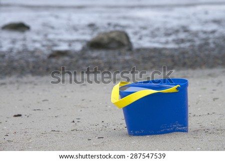 blue bucket abandoned at the beach full of water from the last high tide