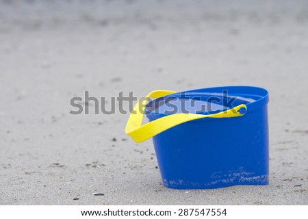 blue bucket abandoned at the beach full of water from the last high tide