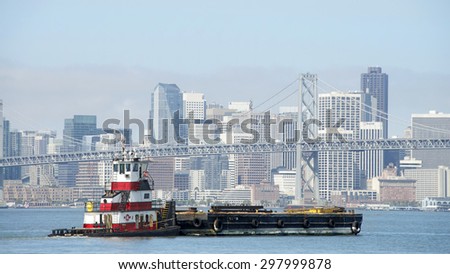 OAKLAND, CA - JULY 13, 2015: Tugboat BAYCAT pushing a barge ship through the San Francisco Bay to the Port of Oakland. A tugboat maneuvers vessels by pushing or towing them.