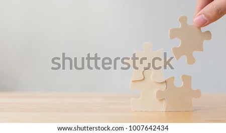Hand of male or female putting jigsaw puzzle connecting on wooden desk and wall background, Strategic management and business solutions for success