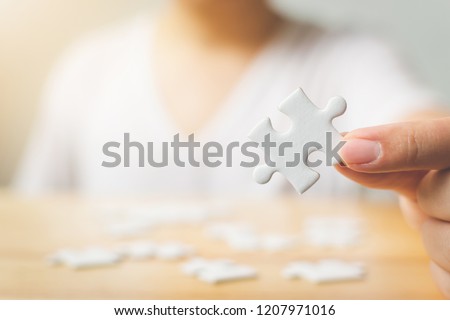 Hand of male trying to connect pieces of white puzzle on wooden table. Healthcare for alzheimer disease, dementia, memory loss, autism awareness and mental health concept