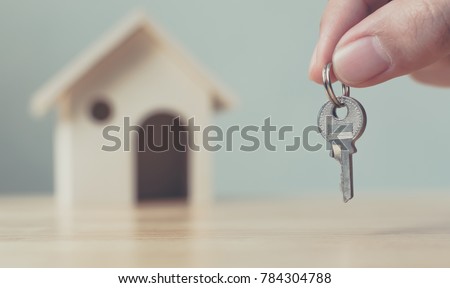Hand holding house key with wooden home background blurred, Real estate and property investment and house mortgage financial concept
