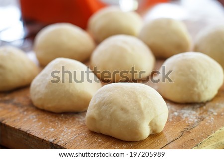Small balls of fresh homemade pizza dough on floured wooden board