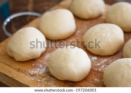 Small balls of fresh homemade pizza dough on floured wooden board