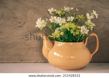 Flower in a yellow tea pot on wooden background, cozy home rustic decor, cottage living