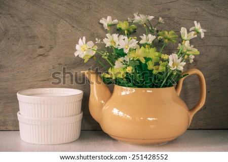 Flower in a yellow tea pot and two white cup on wooden background, cozy home rustic decor, cottage living