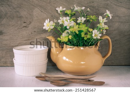 Flower in a yellow tea pot and two white cup and wood spoon on wooden background, cozy home rustic decor, cottage living