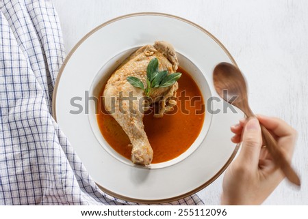 Red curry chicken served in a white plate with girl hand moving catch wood spoon, Delicious and famous Thailand food