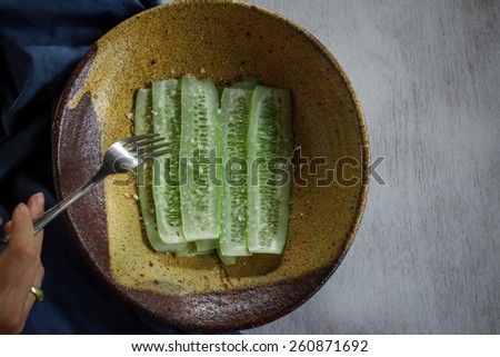 Slices of cucumber with sea salt served on old yellow plate and moving hand, still life image