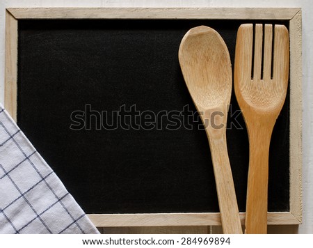 Blackboard on wooden surface with napkin and serving spoons