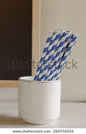Blue and white straws paper in white cup. Image soft focus and soft tone.