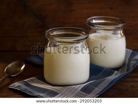Greek yogurt in a glass jars on wooden background, still life image dark tone.