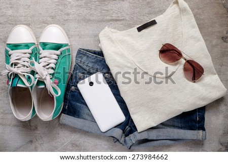 Overhead of essentials of a modern woman. Outfit of casual woman. shoes shirt jean shorts sunglasses , cell phone