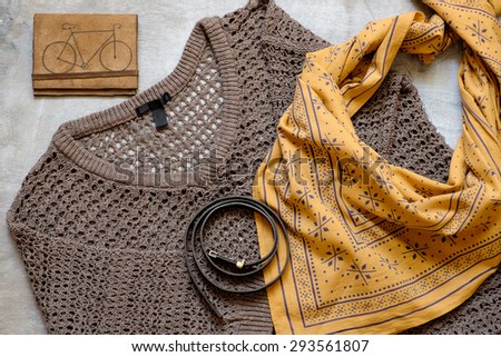 Outfit of casual woman. Brown sweater and a yellow scarf leather wallet belt on a wooden background.