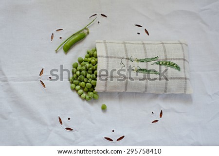 Bag of linen with embroidery cross with green peas on a white vintage tablecloth